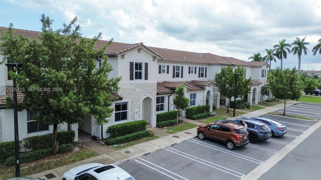 Multi-story townhouse exterior featuring a light-toned stone facade, tiled roofing, decorative shutters, and manicured shrubbery