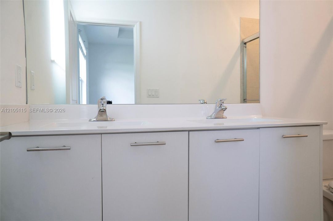Dual-sink vanity with a solid-surface countertop, integrated rectangular basins, polished chrome faucets, and minimalist flat-panel cabinetry