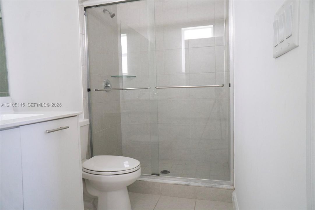 Walk-in shower featuring a glass sliding enclosure, tile wall surround, and integrated shelving, complemented by a white vanity cabinet and ceramic tile flooring