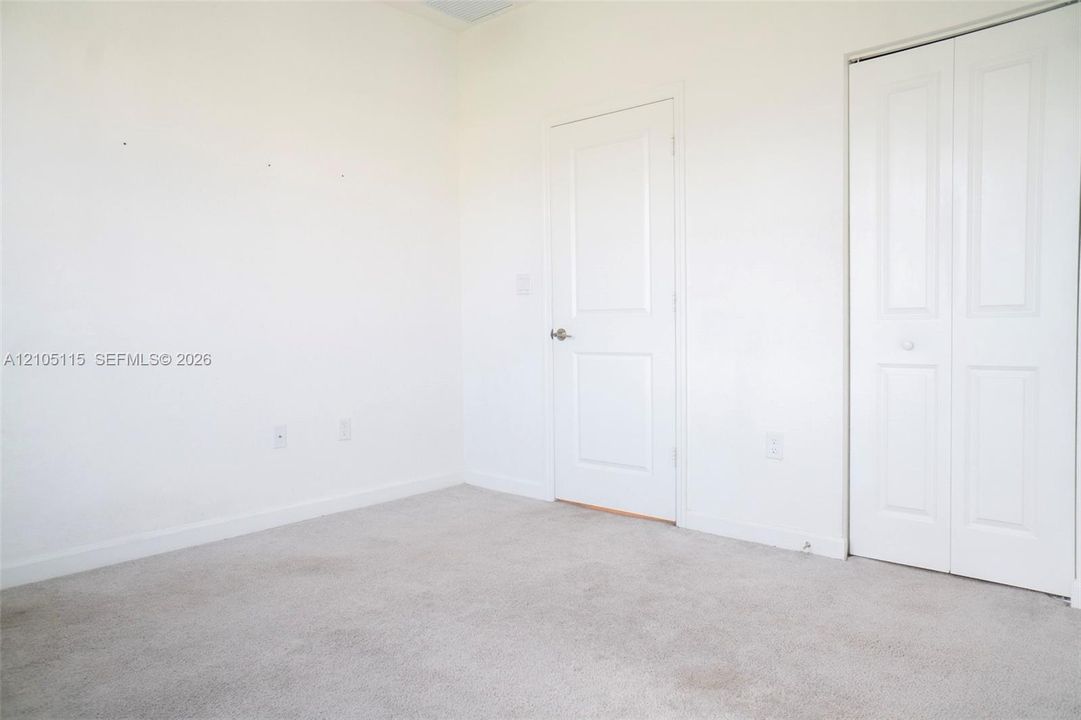 Room featuring neutral wall-to-wall carpeting, white interior paint, a two-panel interior door with a brushed nickel handle, and a double-door closet