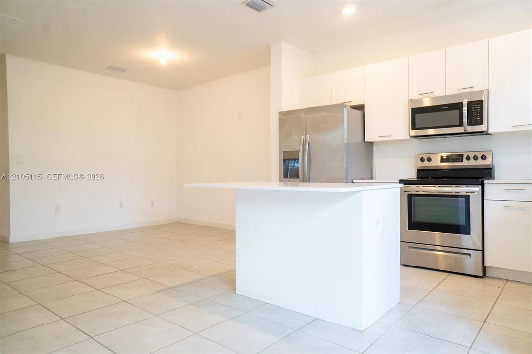 Kitchen featuring white cabinetry, an island with a solid surface countertop, stainless steel appliances, and tile flooring