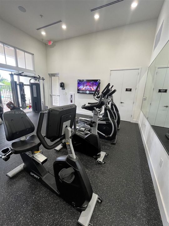 Fitness room featuring high ceilings, rubberized flooring, wall-mounted television, and floor-to-ceiling mirror