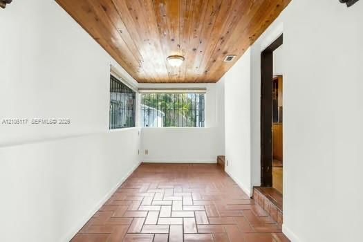 Tongue-and-groove wood-paneled ceiling, terracotta tile flooring in a herringbone pattern, and large windows with integrated security bars