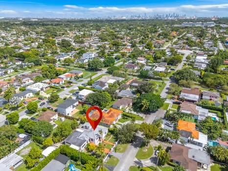 Aerial perspective showcasing a residential property with a tiled roof, situated within a suburban neighborhood featuring mature canopy trees and distant metropolitan skyline