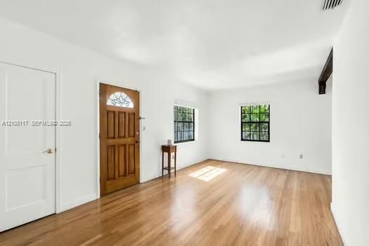 Wood-finish flooring, white walls, wood-paneled entry door with decorative glass inlay, and grid-pattern window panes