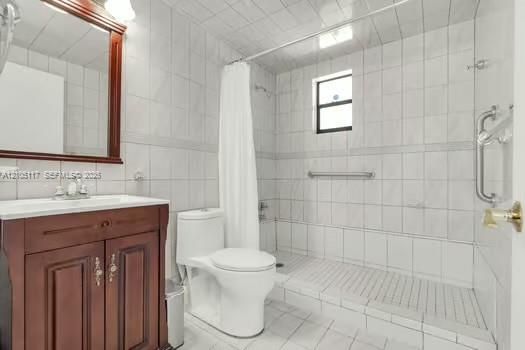 Full-height tiled bathroom featuring a walk-in shower with grab bars, a cherry-wood finish vanity, and a framed wall mirror