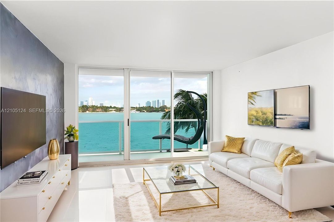 Expansive sliding glass doors open to a balcony with glass railings, showcasing water and city views