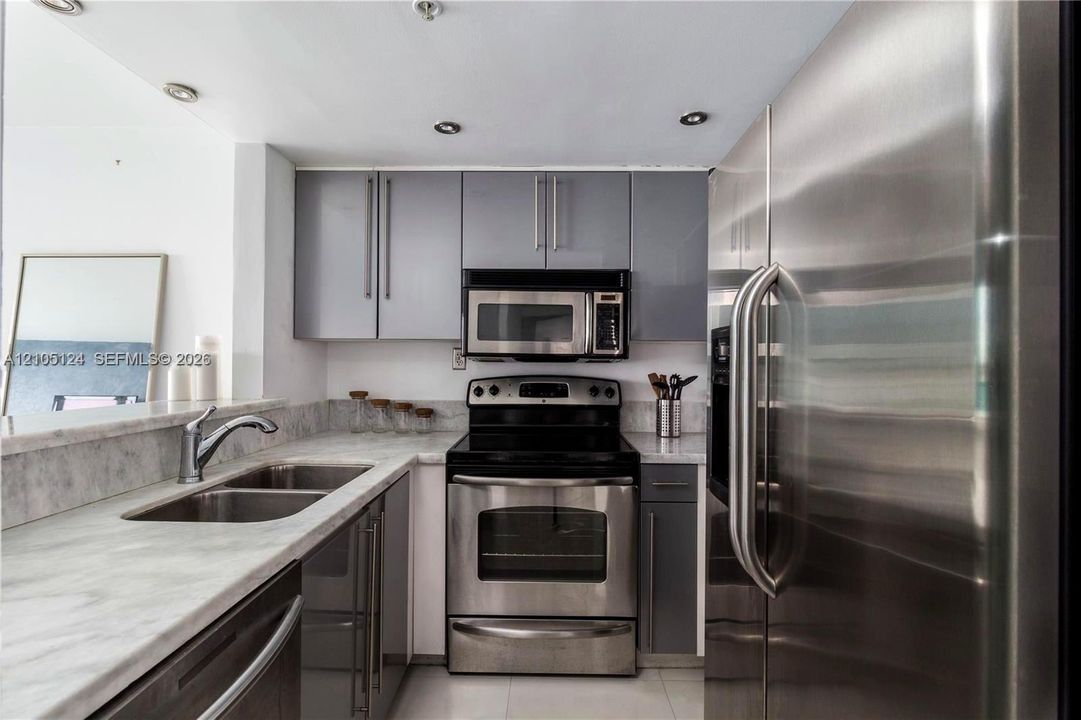 Kitchen featuring stainless steel appliances, grey cabinetry, light-toned stone countertops, and recessed lighting