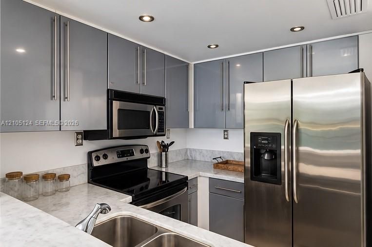 Modern kitchen featuring sleek gray cabinetry, stainless steel appliances, recessed lighting, and light-toned countertops