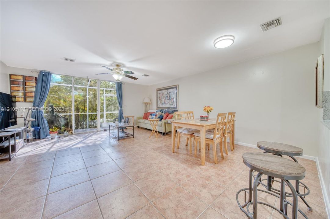 Tiled flooring throughout, featuring a dining area, a ceiling fan with integrated lighting, and a large window wall