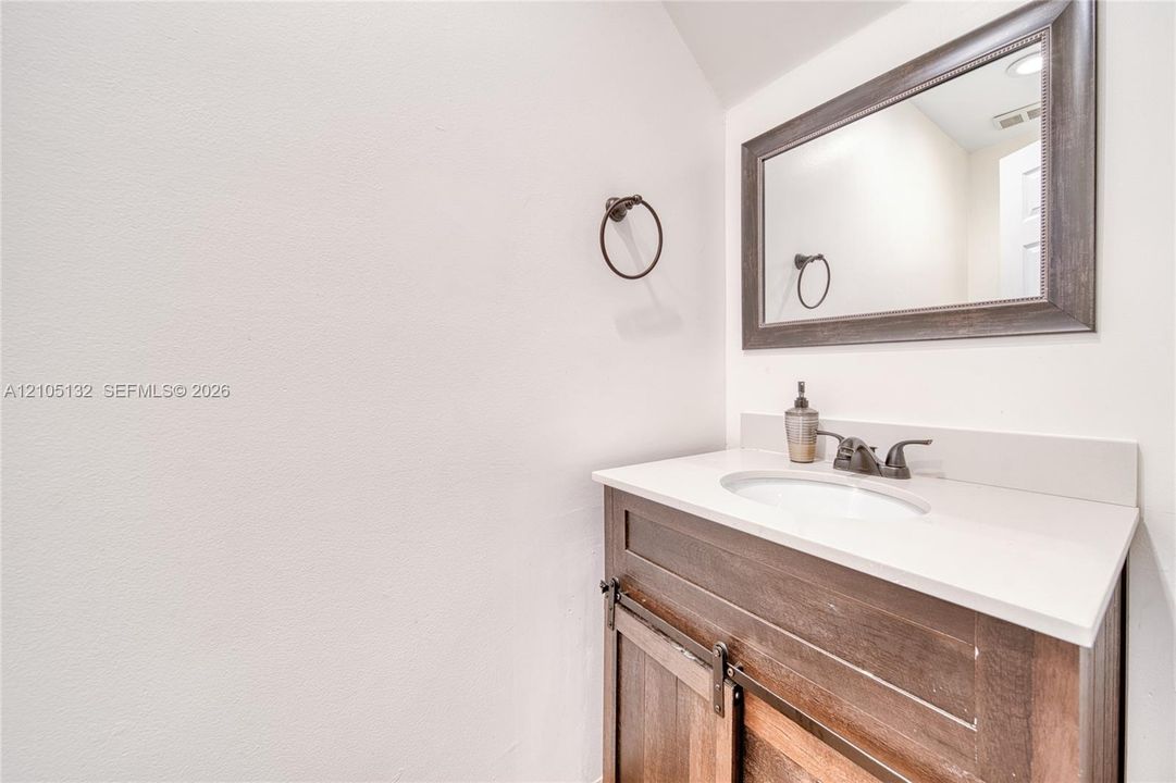 Vanity with wood-finish cabinetry, white countertop, and integrated sink