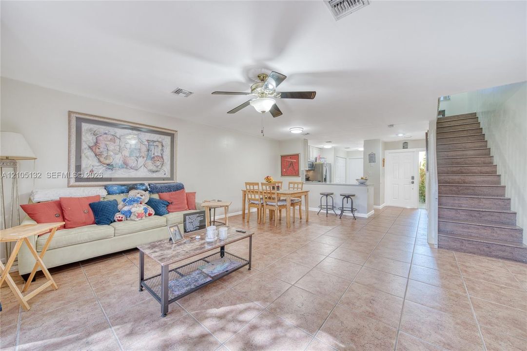 Open-concept living area with tile flooring, a ceiling fan, and a breakfast bar