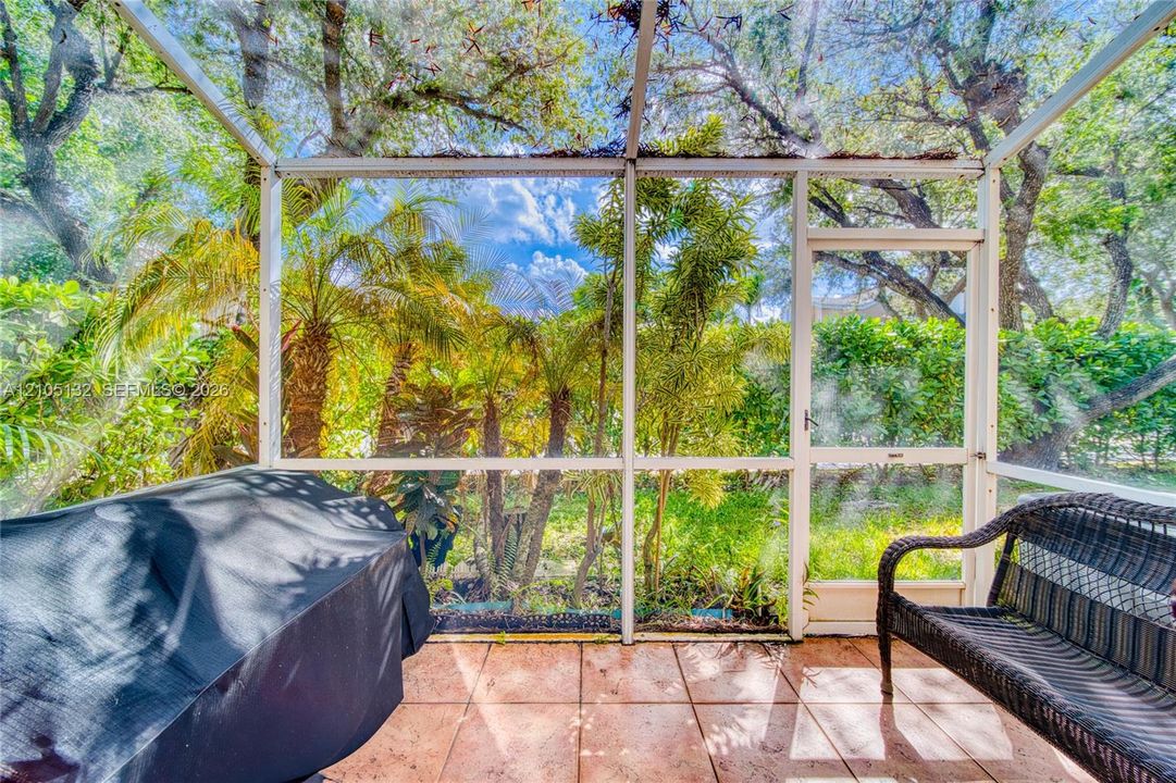 Screened-in outdoor enclosure with a tiled floor, framed by lush foliage and mature trees