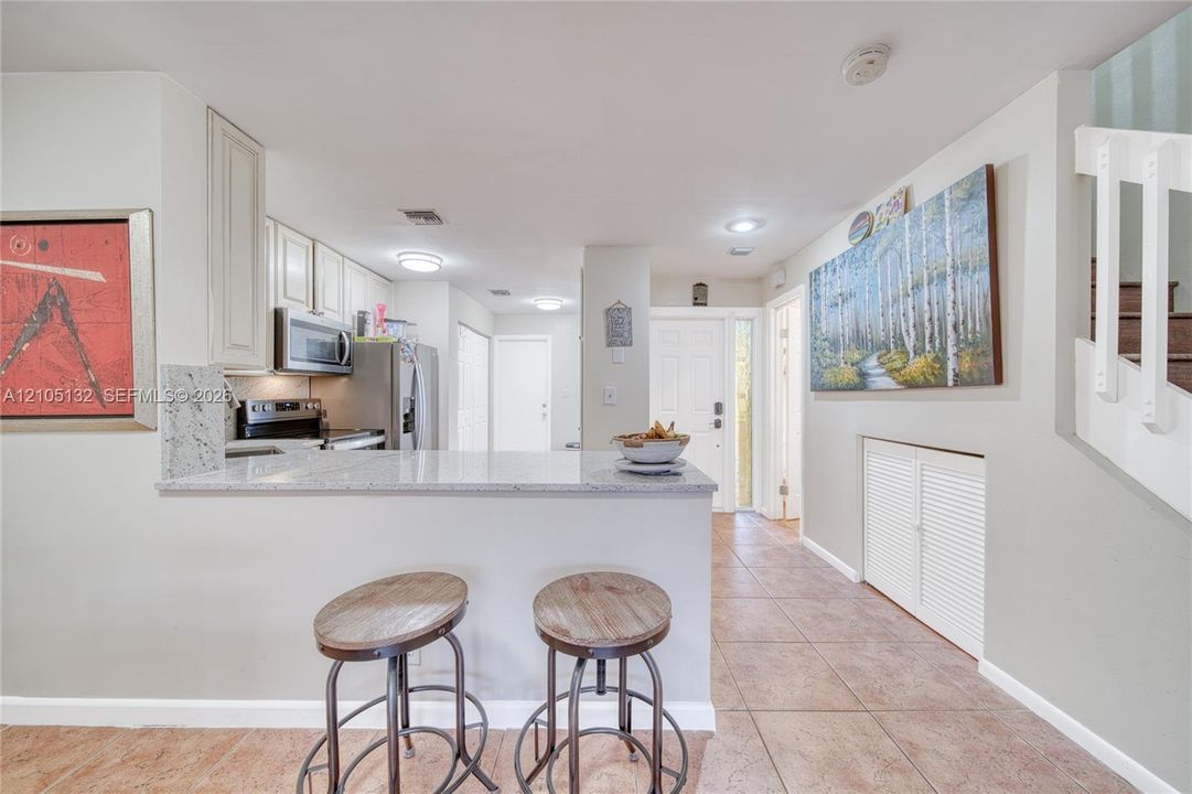 Kitchen pass-through with a light-toned countertop, white cabinetry, stainless steel appliances, and tile flooring