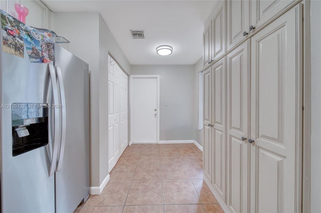 Extensive built-in cabinetry with panel doors, stainless steel refrigerator, tile flooring, and flush mount lighting