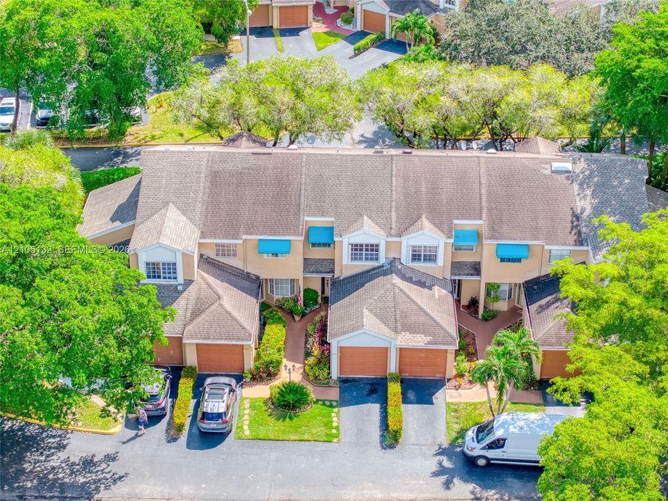 Multi-unit property featuring individual garages, paved driveways, and mature landscaping