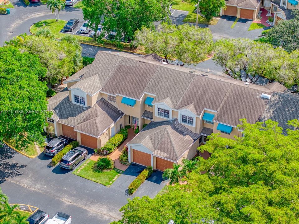 Townhome-style residences featuring light-toned exteriors, pitched shingle roofs, individual garages, and blue fabric awnings