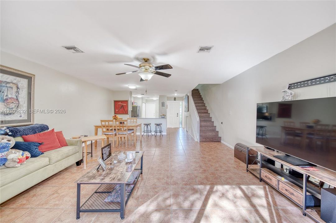 Open concept living area with tile flooring, ceiling fan, and stairwell with wood-finish treads