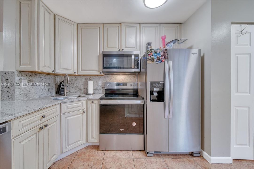 White cabinetry, light-toned countertops, stainless steel appliances, tile flooring, and integrated sink