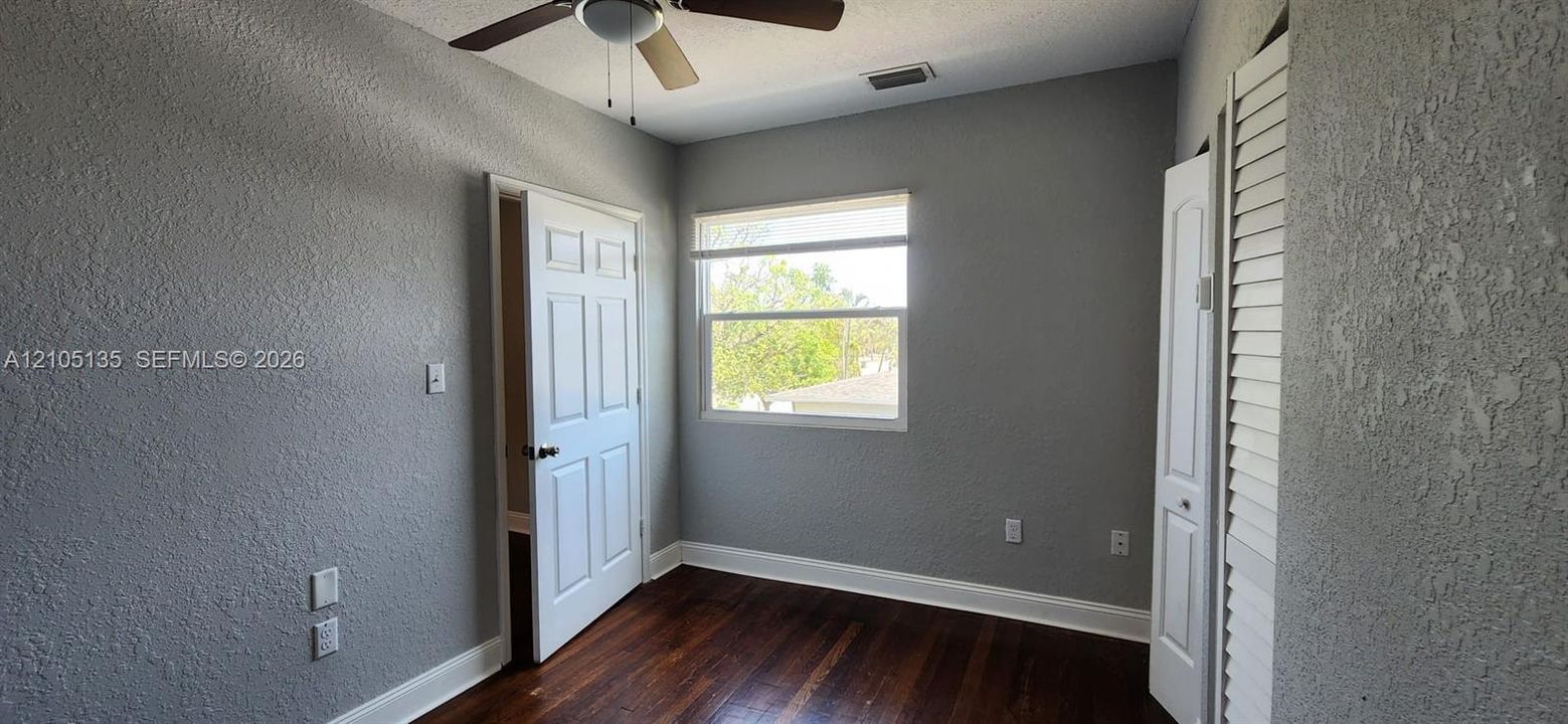 Wood-finish flooring with white trim, a ceiling fan, and a window with a white frame