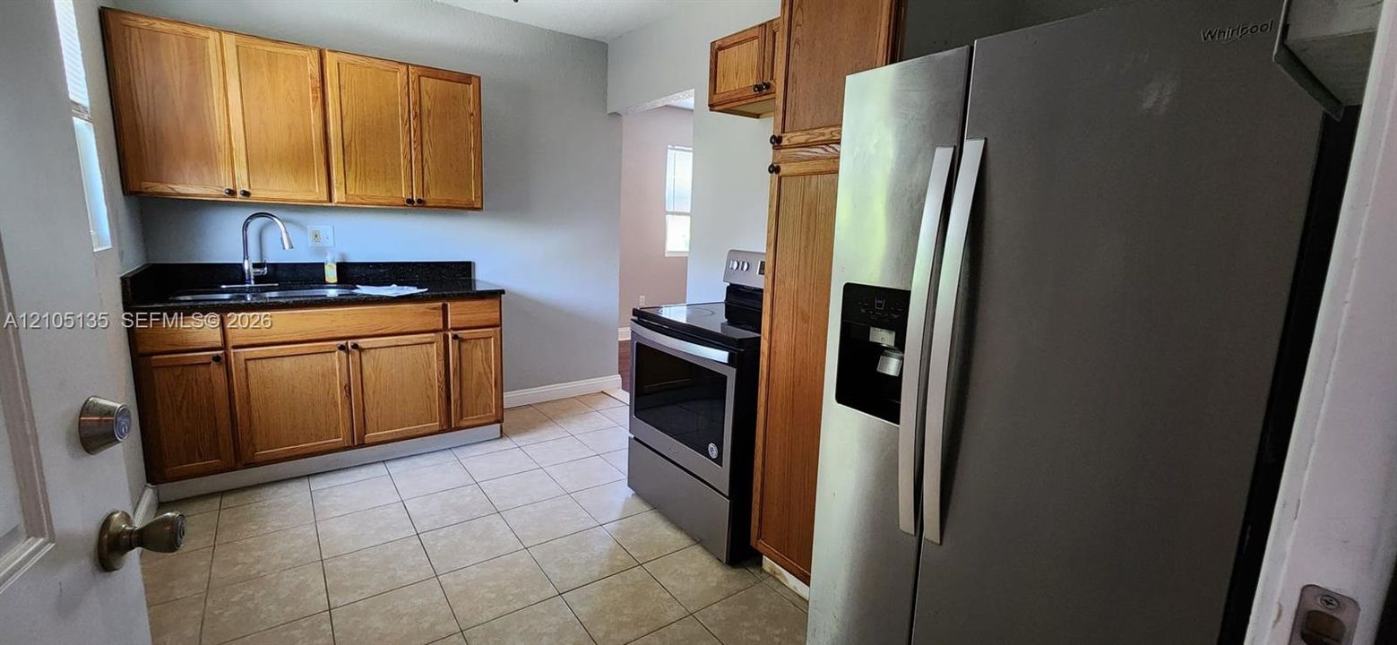 Kitchen featuring wood cabinetry, stainless steel appliances, dark countertop, and tiled flooring