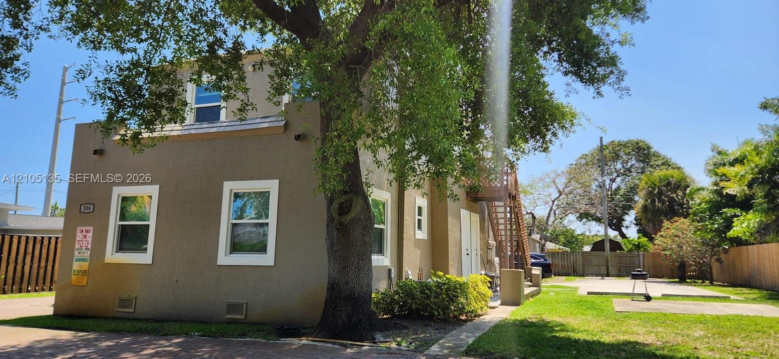 Stucco exterior with white-framed windows, mature tree, manicured lawn, and paved patio area