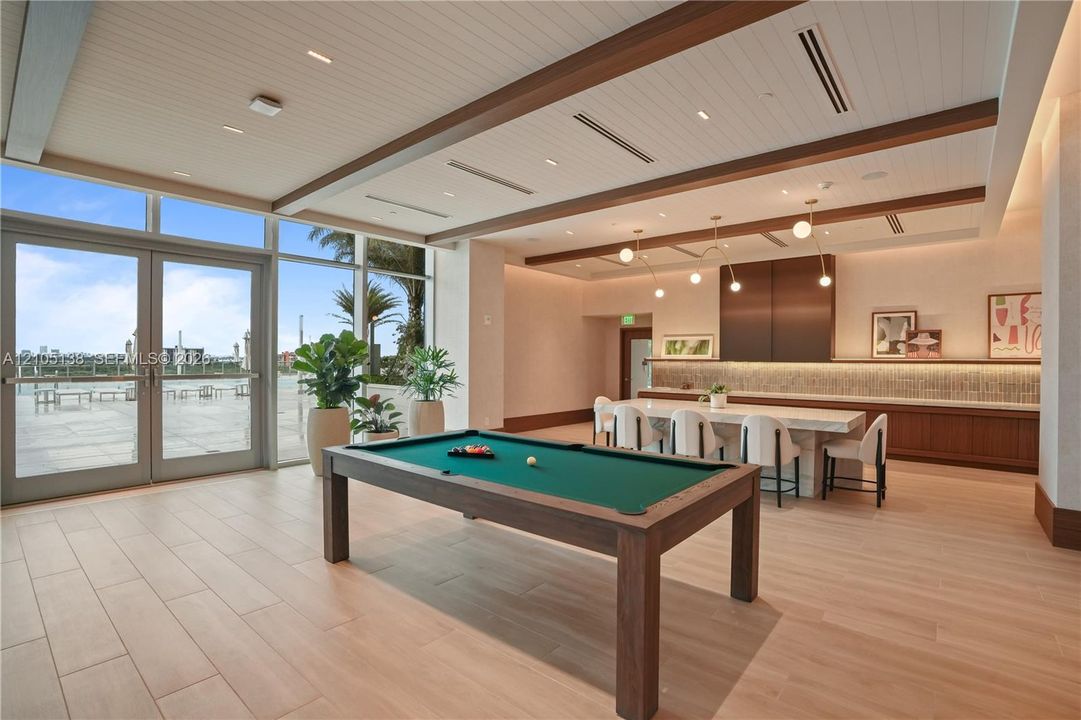 Spacious entertainment area with large format tile flooring, a built-in buffet with wood-finish cabinetry, a decorative accent wall, and expansive glass doors opening to an exterior patio