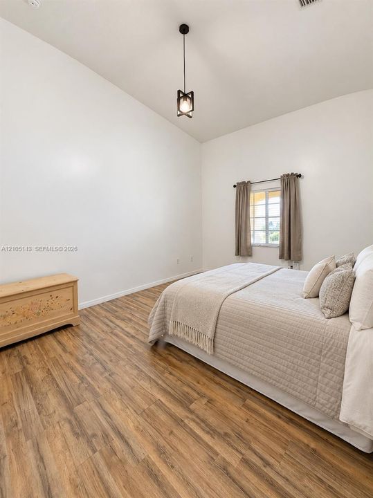 Vaulted ceiling with a contemporary pendant light fixture, wood-finish flooring, and a window with natural light