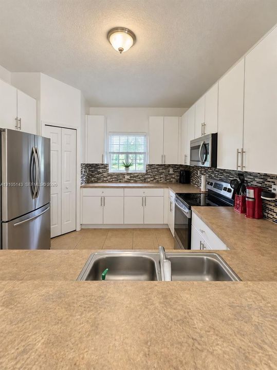 Kitchen featuring a double basin stainless steel sink, light-toned countertops, white cabinetry, and stainless steel appliances