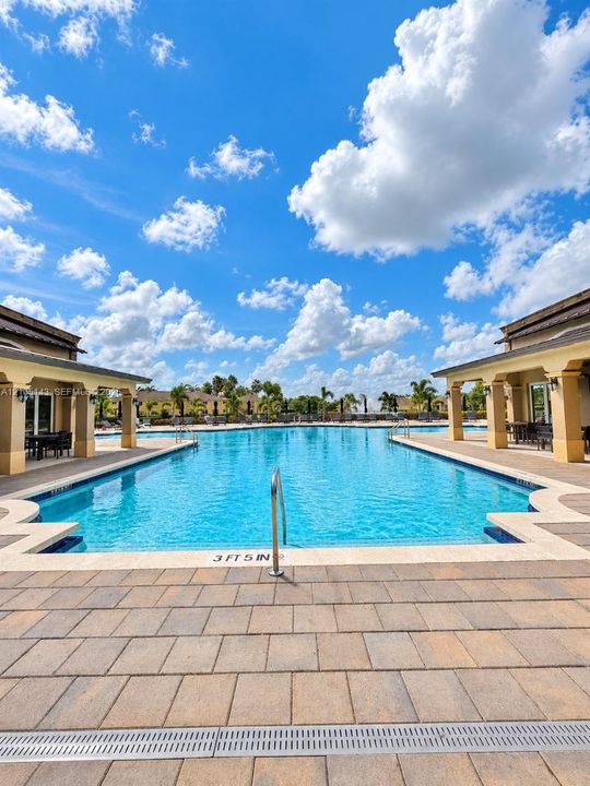 Expansive outdoor pool area with a large swimming pool, surrounding paver patio, covered seating areas, and lush landscaping