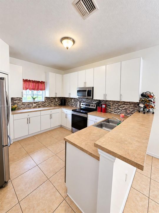 Kitchen featuring white cabinetry, tile flooring, stainless steel appliances, a double basin sink, and a multi-toned backsplash