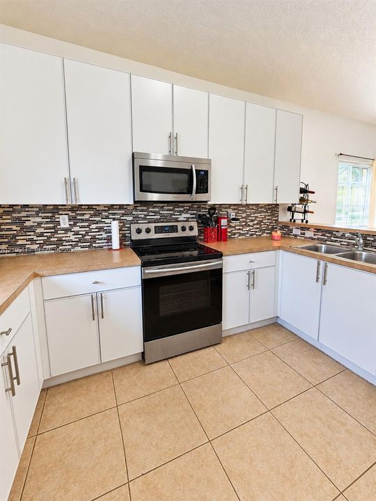 White cabinetry with brushed nickel hardware, stainless steel appliances, tile backsplash, and light-toned countertops
