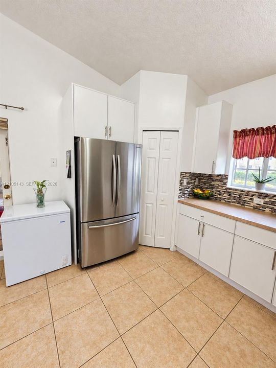 Vaulted ceiling kitchen featuring white cabinetry, stainless steel refrigerator, and tiled flooring