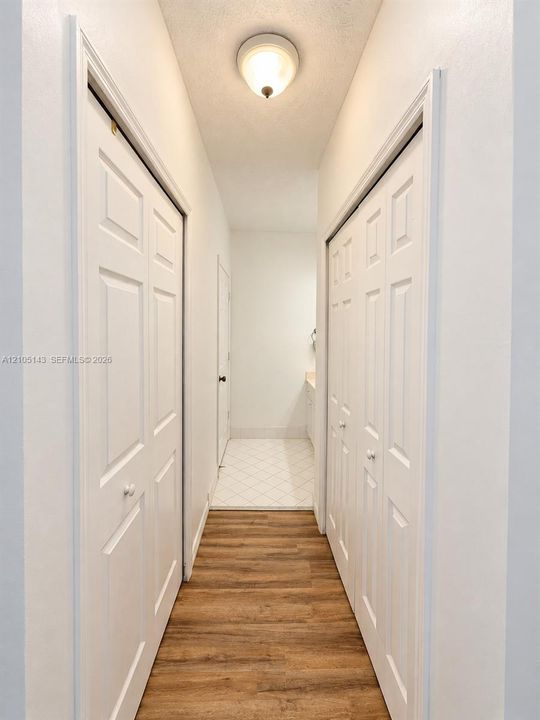 Wood-finish flooring leading to an interior space with white tile flooring and a built-in vanity