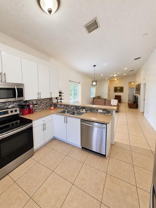 Kitchen featuring a stainless steel appliance suite, white cabinetry with brushed nickel hardware, a mosaic tile backsplash, and light-toned tile flooring