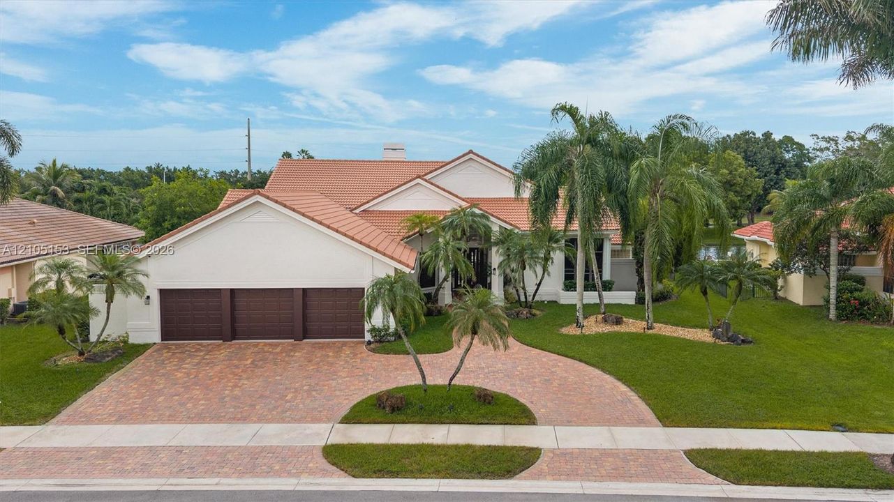 Stucco exterior with a tile roof, three-car garage, brick paver driveway, and mature landscaping