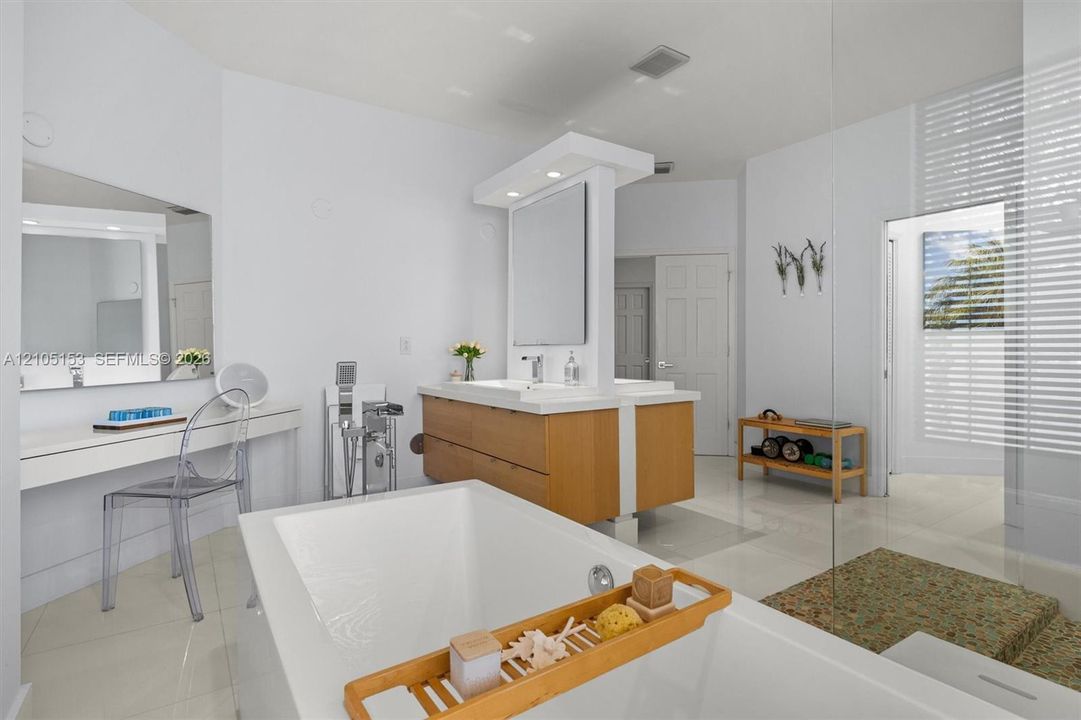 Freestanding bathtub with deck-mounted faucet, dual vanity with wood-finish cabinetry, built-in makeup vanity, glass-enclosed shower, and tiled flooring