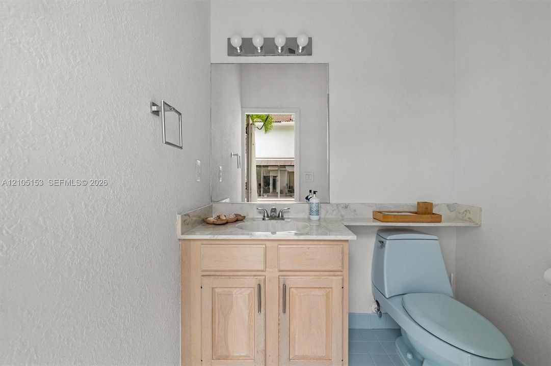 Vanity with a light wood-finish cabinet and stone-look countertop, a large wall-mounted mirror, and a four-bulb vanity light fixture