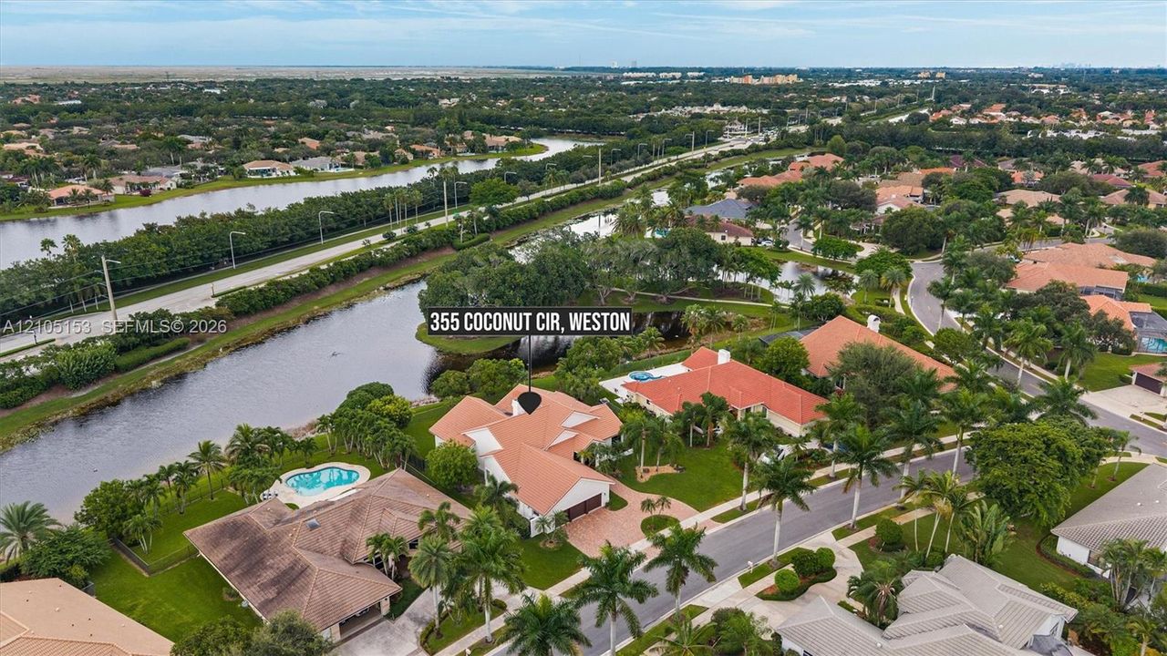 Aerial perspective of a residential neighborhood featuring waterways, mature trees, and individual properties with swimming pools and red tile roofs