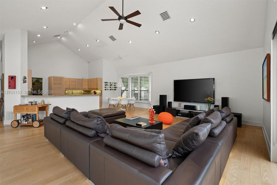 Vaulted ceiling with recessed lighting, wood-finish flooring, ceiling fan, kitchen with light wood-finish cabinetry, and a breakfast bar