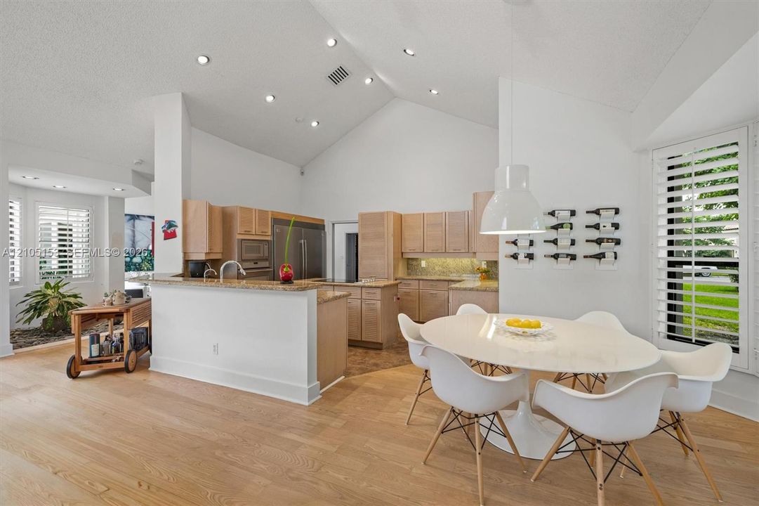 Vaulted ceilings with recessed lighting, wood-finish flooring, kitchen with light wood cabinetry, stone countertops, and stainless steel appliances