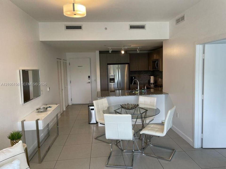 Open-concept interior featuring light tile flooring, stainless steel appliances, neutral cabinetry, and a peninsula island with stone surfacing