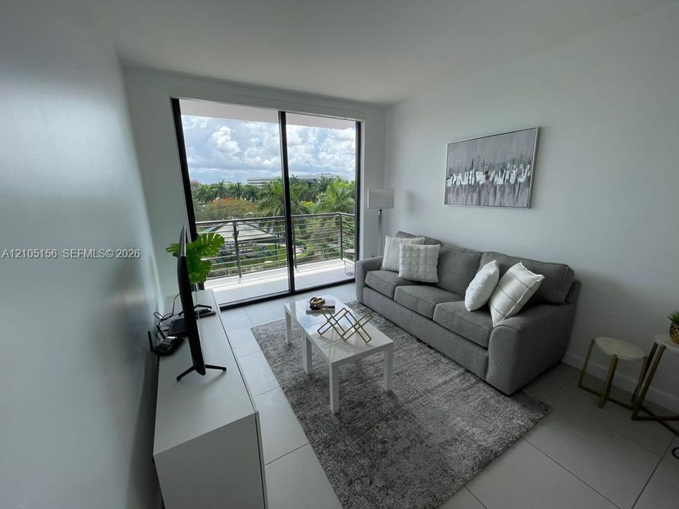 Floor-to-ceiling sliding glass doors, neutral tile flooring, and private balcony with horizontal railing