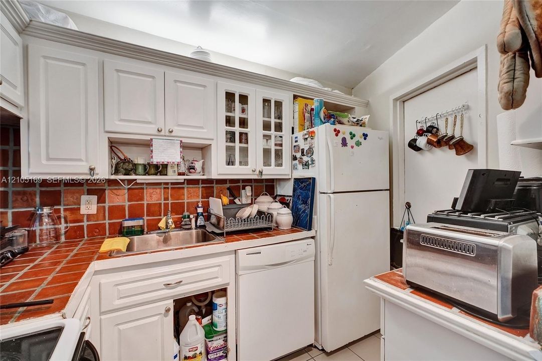 White cabinetry with glass-front accents, stainless steel sink, and a red tile backsplash