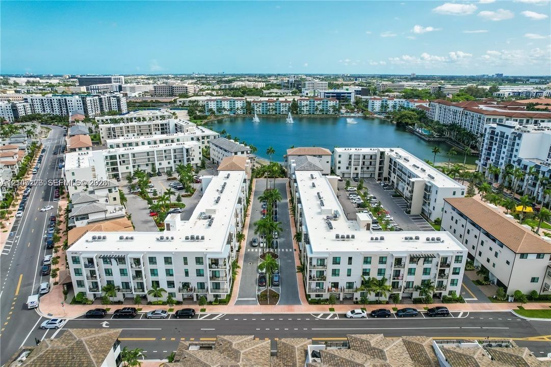 Aerial perspective of a multi-story residential complex featuring white stucco facades, flat roofs, surface parking, and palm tree-lined paved thoroughfares