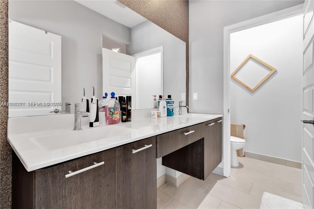 Floating vanity featuring dark wood-finish cabinetry, a wide countertop with dual integrated sinks, polished chrome fixtures, and a wall-to-wall mirror