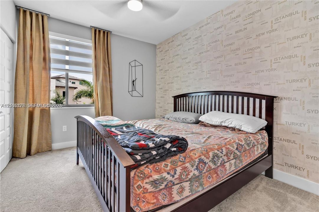 Room featuring neutral carpeting, a patterned accent wall, and a ceiling-mounted light fixture with a fan