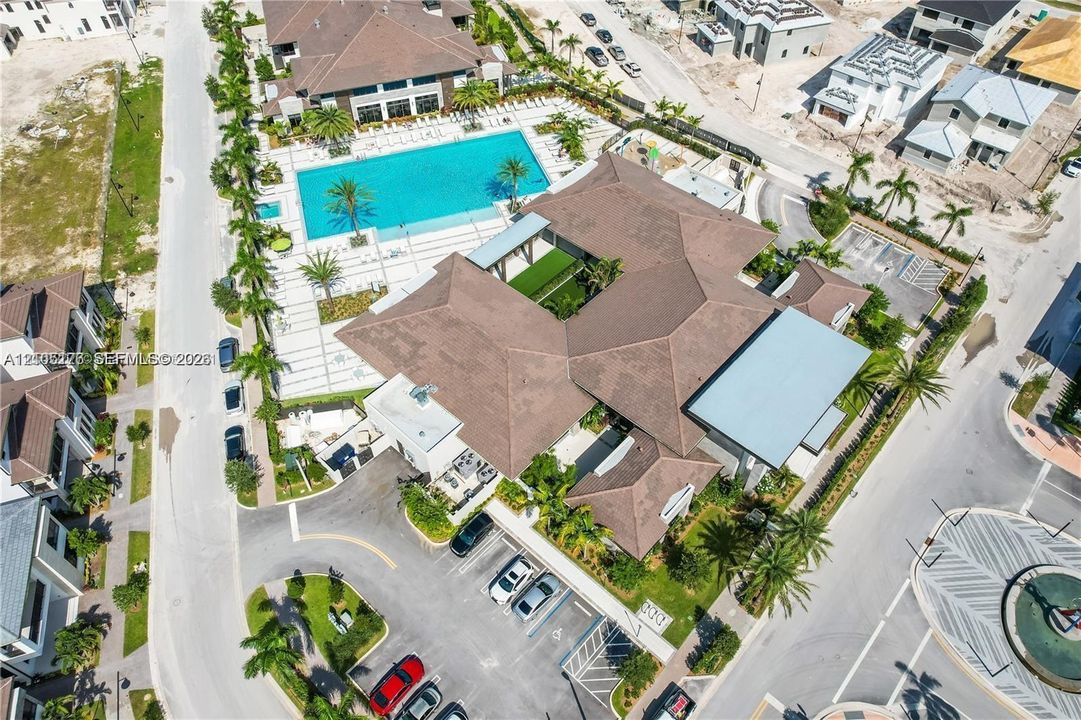 Aerial perspective of a multi-structure complex featuring a swimming pool, paved sundeck, surface parking, landscaped grounds, and a central courtyard
