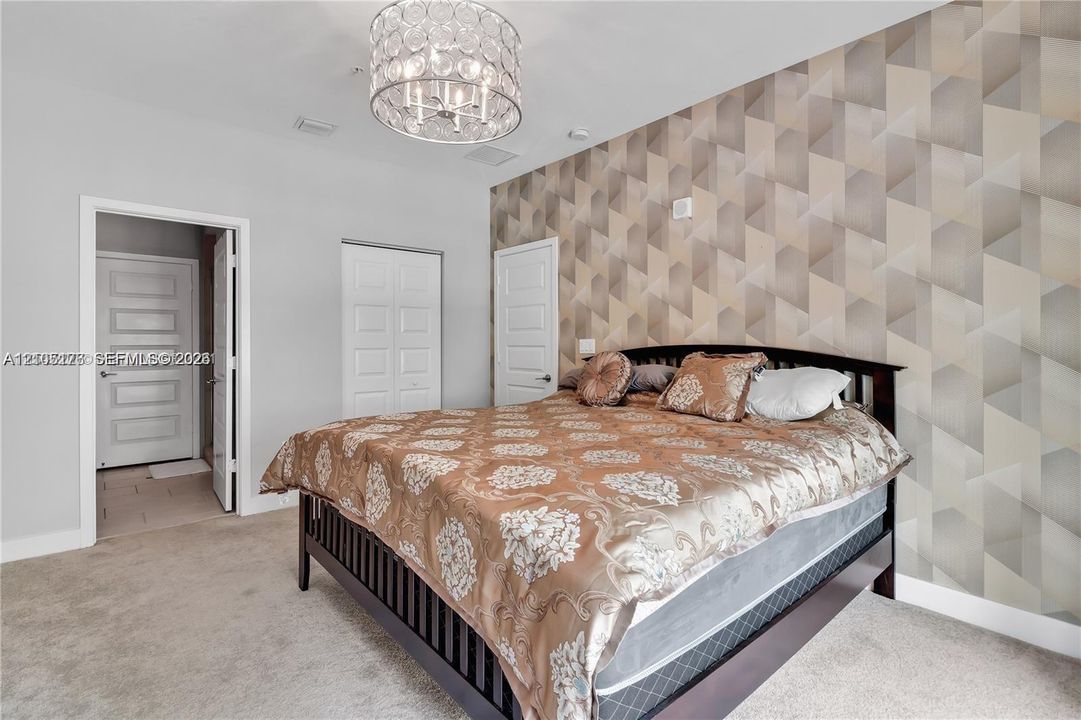 Geometric pattern accent wall, crystal-embellished drum chandelier, neutral carpeting, and multi-panel interior doors