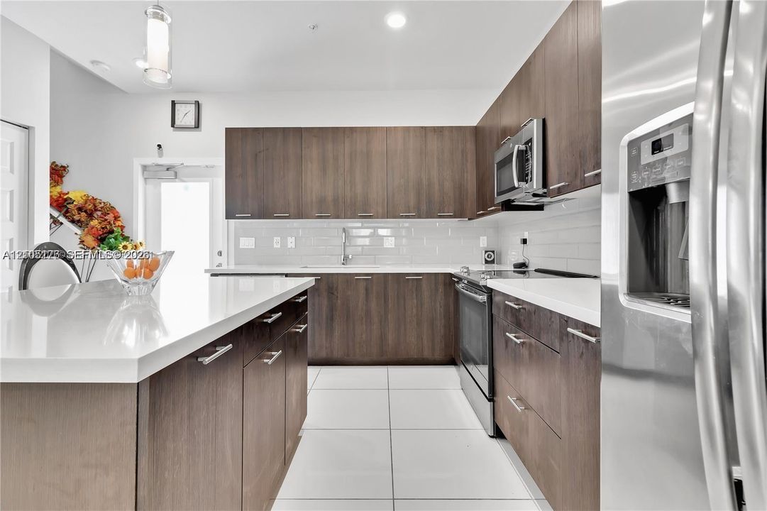 Kitchen featuring flat-panel wood-finish cabinetry, white countertops, stainless steel appliances, subway tile backsplash, and large-format floor tile